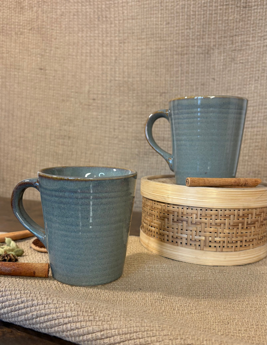 Two blue ceramic mugs on a textured surface with a woven basket.